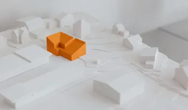 A white architectural scale model of a neighbourhood, with one building picked out in orange