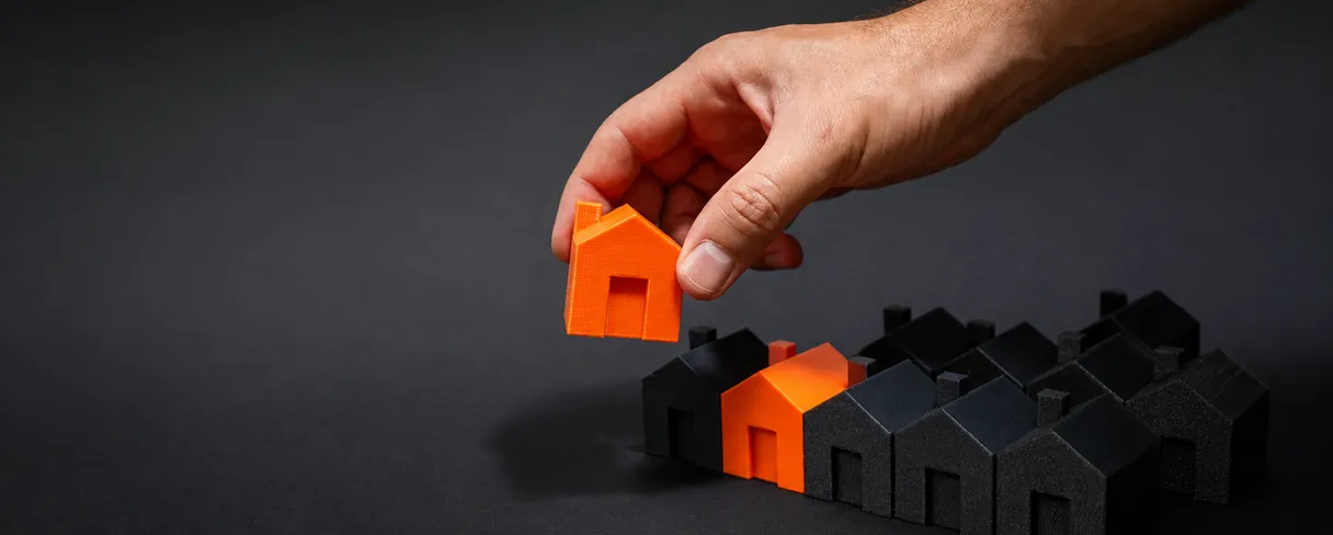 A hand placing an orange model house among black model houses