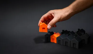 A hand placing an orange model house among black model houses