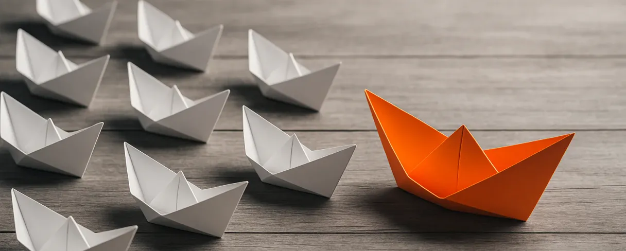 An orange paper boat leading a group of white paper boats