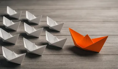 An orange paper boat leading a group of white paper boats
